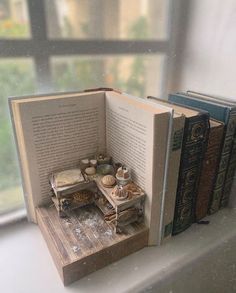 an open book sitting on top of a window sill next to books and cups