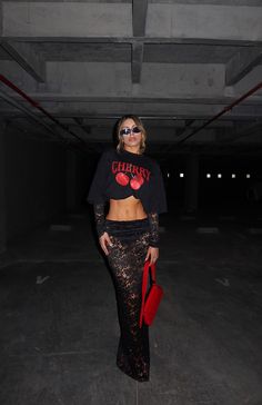 a woman in a black crop top and skirt posing for the camera with her red purse