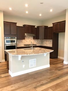 an empty kitchen with wooden floors and white counter tops, along with dark wood cabinets