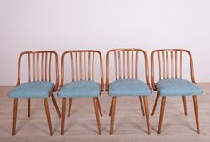 four wooden chairs with blue upholstered seats in front of a white wall and wood floor