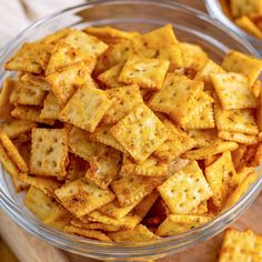 a glass bowl filled with cheesy crackers on top of a wooden cutting board