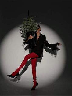 a woman in red pants and black jacket holding a christmas tree