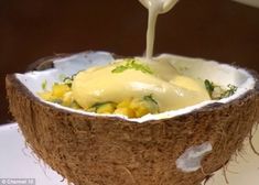 someone pouring sauce into a coconut shell with other food items in the bowl behind it