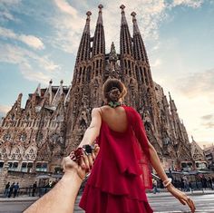 a woman in a red dress holding the hand of a man in front of a tall building