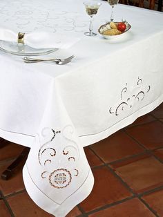 a white table cloth with an embroidered design on it and two wine glasses sitting on the table