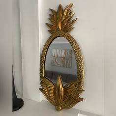 a gold mirror sitting on top of a white counter next to a black vase and lamp