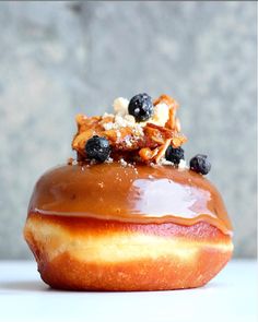 a glazed donut with blueberries and nuts on top, sitting on a table