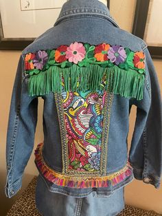 "This jacket is for the child who loves sparkle and frills! The back panel is a 60's print, edged in blue and gold trim. The seam separating the jacket back and yoke is embellished with trim and fringe. The peplum hem is also adorned with mini fringe. Jordache denim jacket Size 5/6 77% cotton, 33% other (unreadable) Snap enclosures Chest 13\" Shoulder 11\" Sleeve 14 1/4\" Length 15\"" Spring Festival Denim Jacket With Fringe, Spring Denim Jacket With Beaded Fringe And Long Sleeves, Fitted Spring Outerwear With Tassels, Fitted Outerwear With Tassels For Spring, Fitted Denim Jacket With Fringe For Spring, Upcycle Denim, Applique Clothes, Mini Fringe, 60s Print