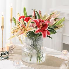 a vase filled with lots of flowers on top of a table next to two candles