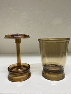 two glass vases sitting next to each other on a white counter top in front of a wall