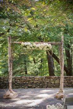 an outdoor ceremony setup with white flowers on the arch and stone wall in the background