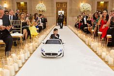 a little boy riding in a toy car on the runway with candles around him and people watching