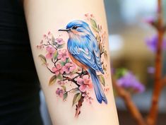 a blue bird sitting on top of a tree branch with pink flowers in the background