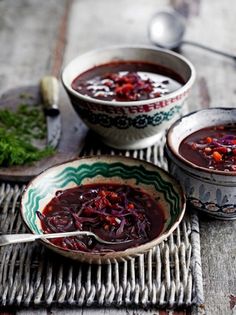 two bowls filled with red cabbage soup on top of a wooden table next to spoons