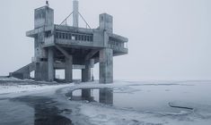 an old concrete structure sitting on top of snow covered ground next to water and ice