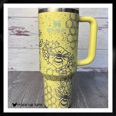 a yellow travel mug with bees and flowers on it is sitting on a wooden table