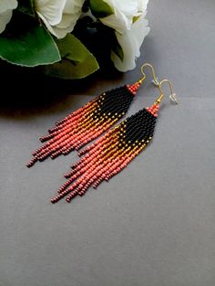 a pair of beaded earrings with flowers in the background on a gray surface next to it