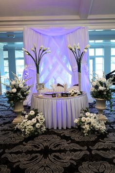 the table is set up with white flowers and centerpieces for an elegant wedding reception