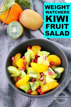 a bowl filled with fruit sitting on top of a gray towel next to an orange and kiwi