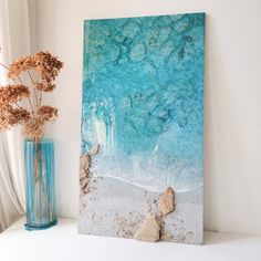 a painting on a shelf next to a vase with flowers in it and a rock