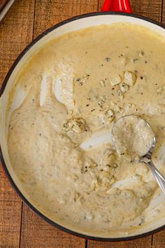 a bowl filled with cream sauce on top of a wooden table next to a spoon