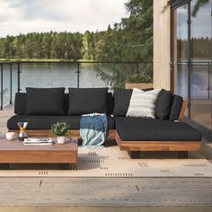 a couch and coffee table on a deck overlooking the water with trees in the background