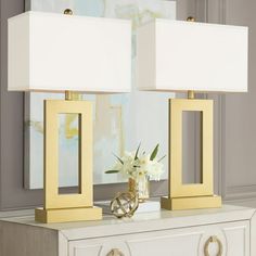 two lamps sitting on top of a dresser next to a vase with flowers in it