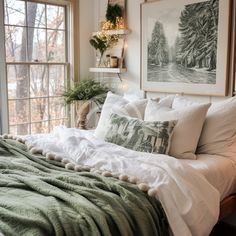 a bed with white linens and green blankets in front of a window that has pictures on the wall above it