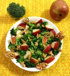 a bowl filled with broccoli, apples and walnuts next to an apple