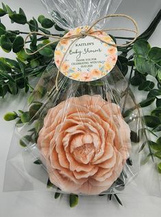 two soap flowers wrapped in cellophane and sitting on top of each other next to some green leaves