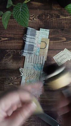 the person is cutting paper with scissors on the wooden table next to some plants and papers