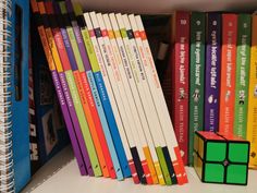 a stack of books sitting on top of a book shelf next to a rubik cube