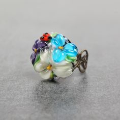 This romantic Glass ladybug flower ring is a perfect gift for women. It's very tender and unique! Set Matching bracelet: https://www.etsy.com/listing/161559547 Matching earrings: https://www.etsy.com/listing/200833152 Matching pendant: https://www.etsy.com/listing/161556072 Dimensions: the ring is adjustable. The bead is 2.2-2.4cm in diameter. Materials: artist lampwork bead, metal fittings. Colors used: blue, white, lilac, violet, green. Please, note, each bead is made by hand and may differ sl Whimsical Adjustable Ring Jewelry, Whimsical Adjustable Ring, Whimsical Adjustable Jewelry Ring, Adjustable Whimsical Ring, Dainty Multicolor Flower Jewelry, Unique Adjustable Flower Jewelry, Whimsical Adjustable Rings, Delicate Flower Ring For Spring Gift, Whimsical Flower-shaped Jewelry