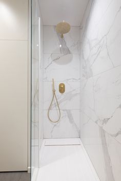 a bathroom with marble walls and flooring, shower head in the corner next to glass door