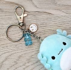 a blue stuffed animal keychain sitting on top of a wooden table next to a button