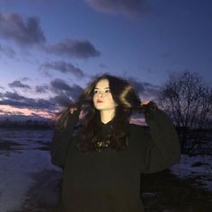 a woman with long hair standing in front of a body of water at sunset or dawn