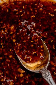 a spoon full of food sitting on top of a white bowl filled with red sauce