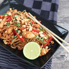 a black plate topped with noodles and vegetables next to chopsticks on a table