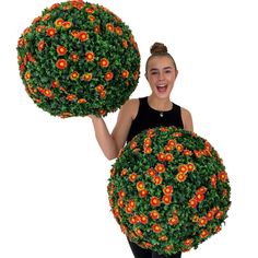 a woman holding two large round bushes with orange flowers