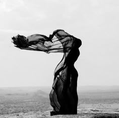 a black and white photo of a woman on top of a hill with her scarf blowing in the wind