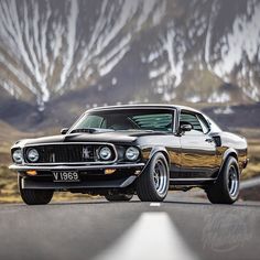 an old muscle car is parked on the side of the road with mountains in the background