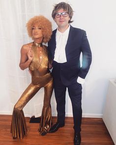 a man and woman dressed up in gold outfits posing for the camera with their arms around each other