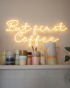 a neon sign that says but first coffee on top of a shelf filled with cups and mugs