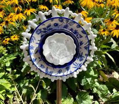 a blue and white plate sitting on top of a wooden stick in front of yellow flowers