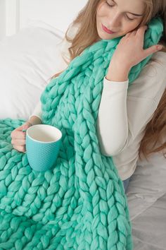 a woman holding a cup and blanket on her bed