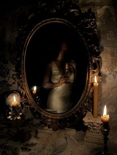 a woman holding a bottle in front of a mirror with candles around it and an ornate frame