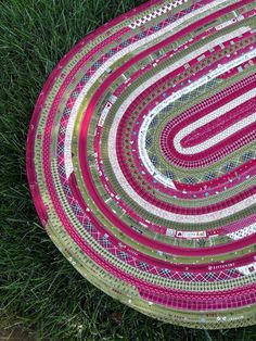 a pink and green circular rug sitting on top of the ground next to some grass