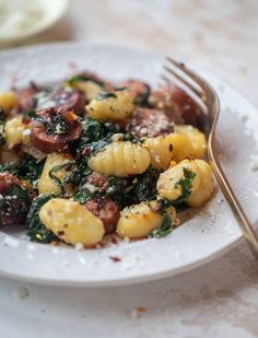 a white plate topped with pasta and spinach next to a fork on top of a table