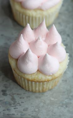 two cupcakes with pink frosting on top sitting on a countertop next to each other