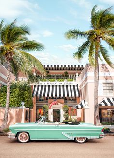 an old green car parked in front of a building with palm trees on the sidewalk